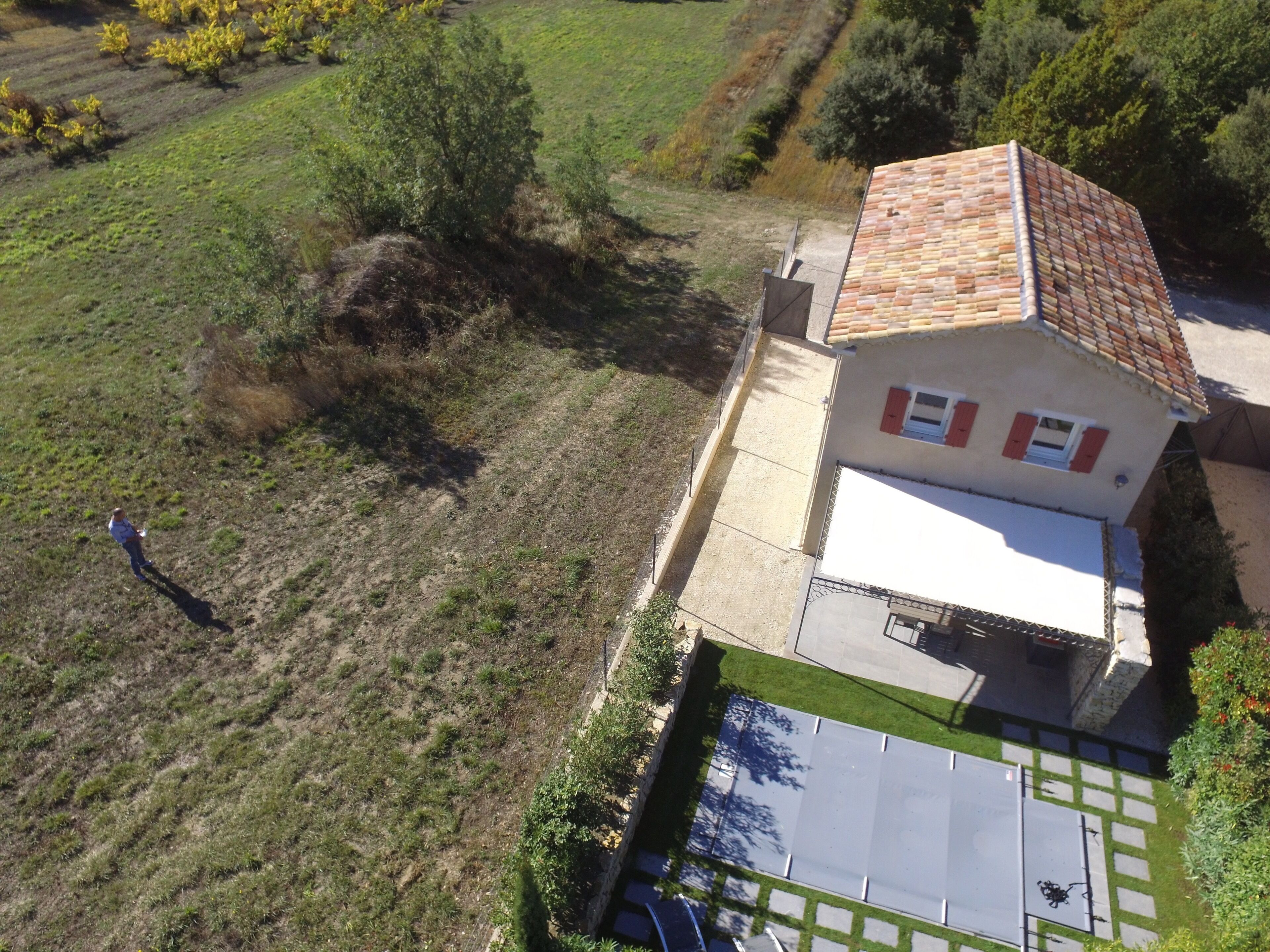 An aerial view of a house with a tiled roof, a small garden, and a paved driveway.