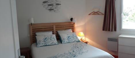 A neatly made bed with a wooden headboard, a bedside lamp, and a wall-mounted shelf with a hanging garment.