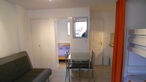 Ein gemütliches Zimmer mit einer Couch, einem kleinen Esstisch mit Stühlen, einem Bett mit Kopfteil und einem Fenster mit Vorhängen.