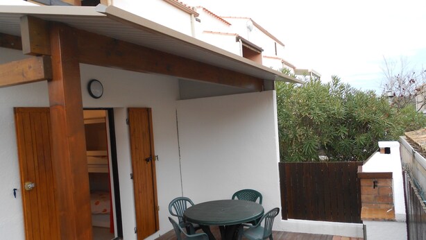 Eine Terrasse mit Tisch und Stühlen, eine Holztür und eine weiße Wand.