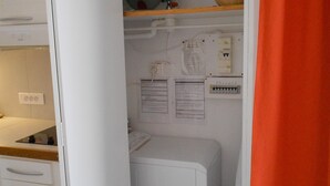 Eine kleine Küche mit Waschmaschine, einer Arbeitsplatte und einem Regal mit einer Schüssel.