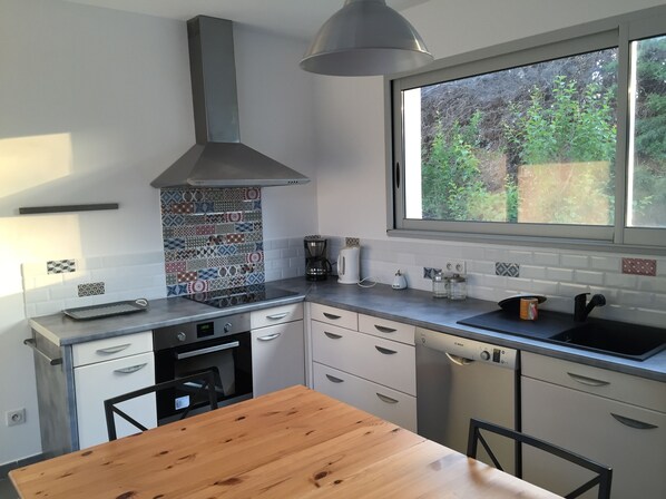 A modern kitchen with a large window, a built-in stove, and a wooden dining table.