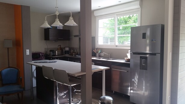 A modern kitchen with a stainless steel refrigerator, a double sink, and a dining area with bar stools. - Bassin d'Arcachon - Beautiful house near the port of Cassy (Lanton)