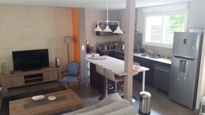 A modern living room with a flat-screen TV, a sofa, a coffee table, and a dining area with a bar stool. - Bassin d'Arcachon - Beautiful house near the port of Cassy (Lanton)