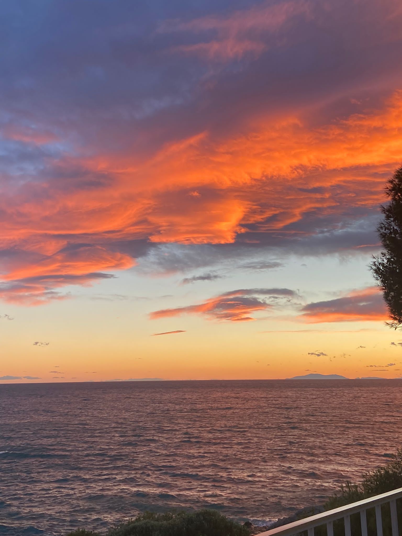 Un coucher de soleil sur l’océan, avec un ciel dégagé et une terre lointaine à l’horizon.