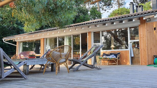 Ein modernes Holzhaus mit großen Fenstern, einer Terrasse mit Gartenmöbeln und einem Garten.