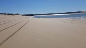 Ein weiter Sandstrand mit blauem Himmel und ruhigem Wasser.