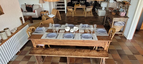 A dining area with a wooden table set for six, surrounded by wicker chairs, and a bench.