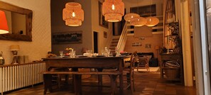 A dining area with a wooden table and chairs, a staircase, and hanging wicker lamps.