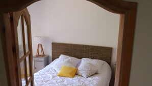Une chambre avec un plancher en bois, un lit avec une literie blanche et un oreiller jaune, et une table de chevet avec une lampe.