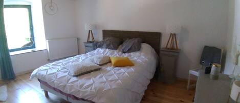 A bedroom with a bed, wooden floor, a white rug, a window with curtains, and a radiator.