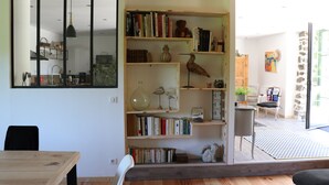 Une pièce avec une bibliothèque en bois remplie de livres, une table à manger avec des chaises et une vue sur l’extérieur.