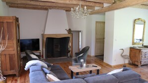 Un salon chaleureux avec un canapé d’angle gris, une table basse en bois, une cheminée et un lustre.