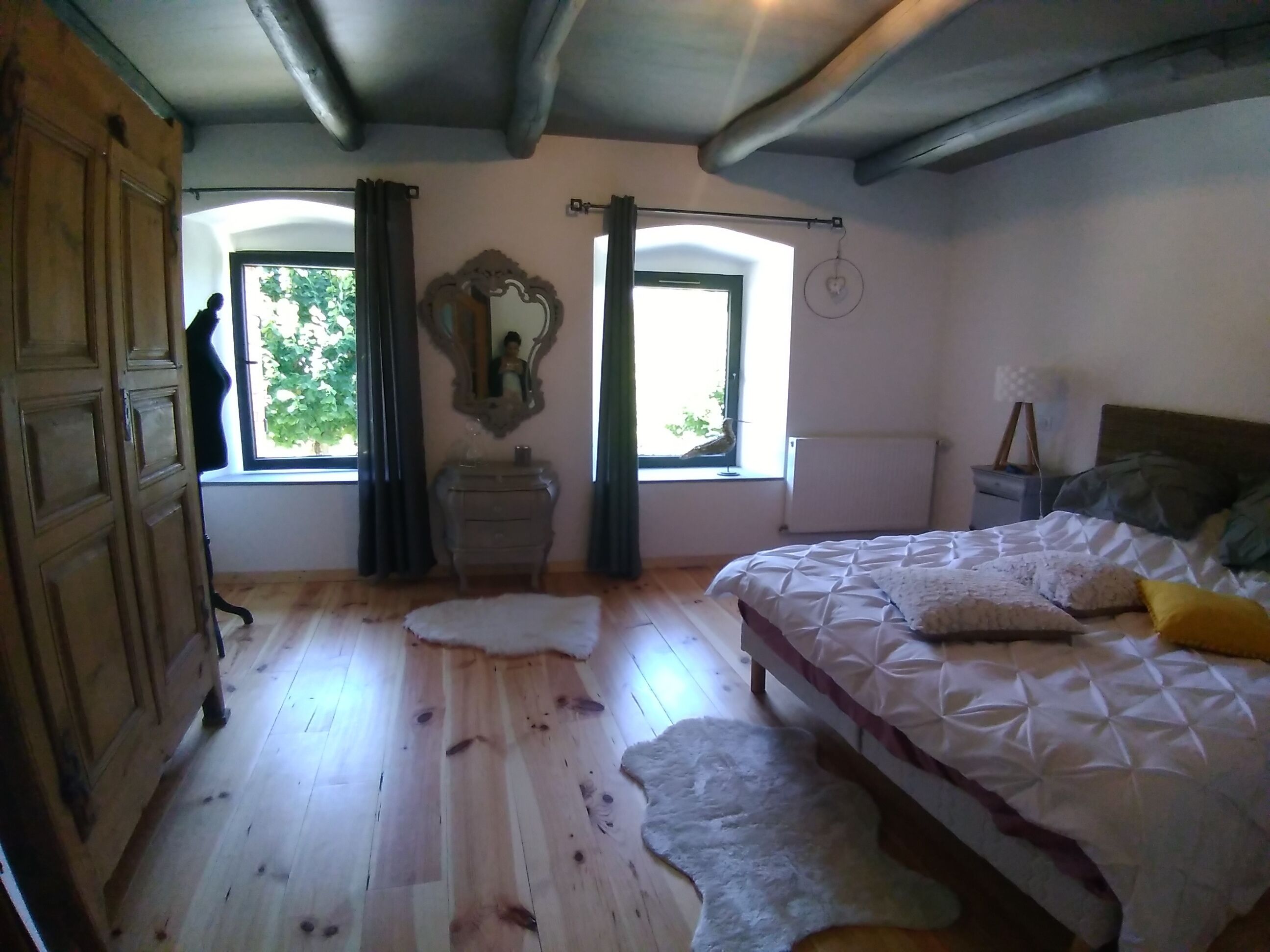 A bedroom with a wooden floor, a bed with a white quilt, a nightstand, a dresser, and a window with curtains.