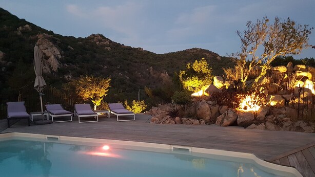 A pool area with lounge chairs and a stone wall.