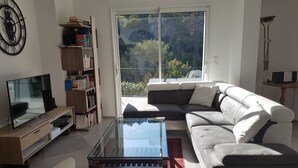 A modern living room with a glass coffee table, a sofa, a TV, and a bookshelf.