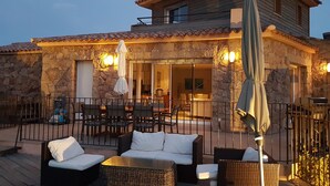 A stone building with a tiled roof, outdoor seating with wicker furniture, and a covered patio area.