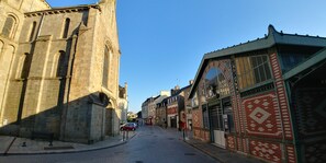 Uma rua estreita com edifícios históricos, incluindo uma igreja com uma alta torre sineira e uma loja com tijolos estampados.