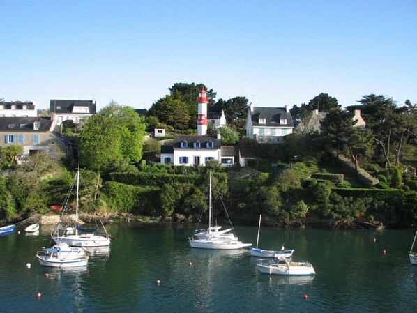 Uma vila costeira com um farol, casas e barcos atracados no porto.