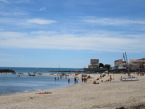 Una playa con piedras, un velero y edificios al fondo.