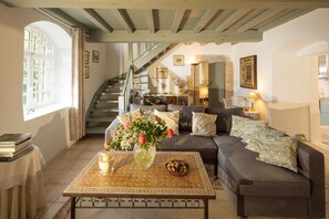 A cozy living room with a sofa, a coffee table with a vase and a muffin, a staircase, and a kitchen area in the background. - Beautifully restored 18th-century mill on the river. (LIEU DIT RAURET)