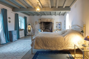 A bedroom with a large bed, a fireplace, a wooden ceiling, and a small table with a lamp. - Beautifully restored 18th-century mill on the river. (LIEU DIT RAURET)