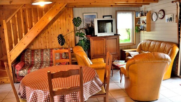 A cozy cabin interior with a wooden staircase, a sofa, a dining table with chairs, a television, and a window with a view. - House                         (Tréguennec)