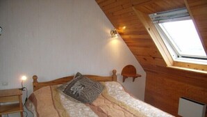A bedroom with a sloped ceiling, a bed with a patterned bedspread, a bedside table, and a small shelf. - House                         (Tréguennec)