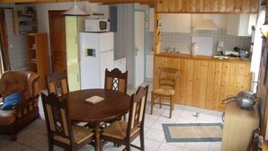 A cozy room with a wooden dining table, chairs, a sofa, a kitchen area with wooden cabinets, a refrigerator, and a microwave. - House                         (Tréguennec)