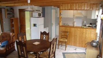 A cozy room with a wooden dining table, chairs, a sofa, a kitchen area with wooden cabinets, a refrigerator, and a microwave.