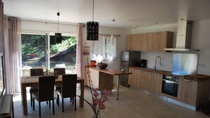 Een moderne keuken met houten kastjes, een inbouwoven en een eethoek met een tafel en stoelen.
