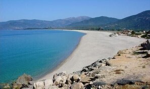 A coastal landscape with a sandy beach, rocky shoreline, and mountains in the background.