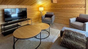Een gezellig houten interieur met een televisie, twee ronde tafels, een bank en twee fauteuils.