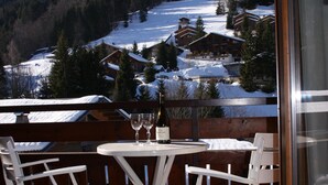 Een balkon met een tafel en stoelen, uitkijkend op een besneeuwd landschap met huizen en bomen.