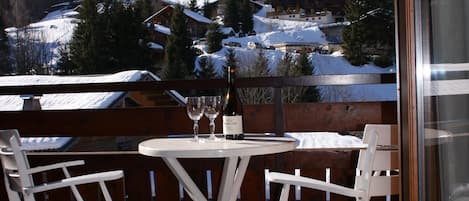 Un balcón con mesa y sillas, con vistas a un paisaje nevado con casas y árboles.