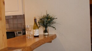 Een keuken met een houten bar, een klok, een fles wijn en twee rieten stoelen.