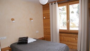 Een slaapkamer met een bed, houten wanden, een raam met gordijnen en een klein nachtkastje.