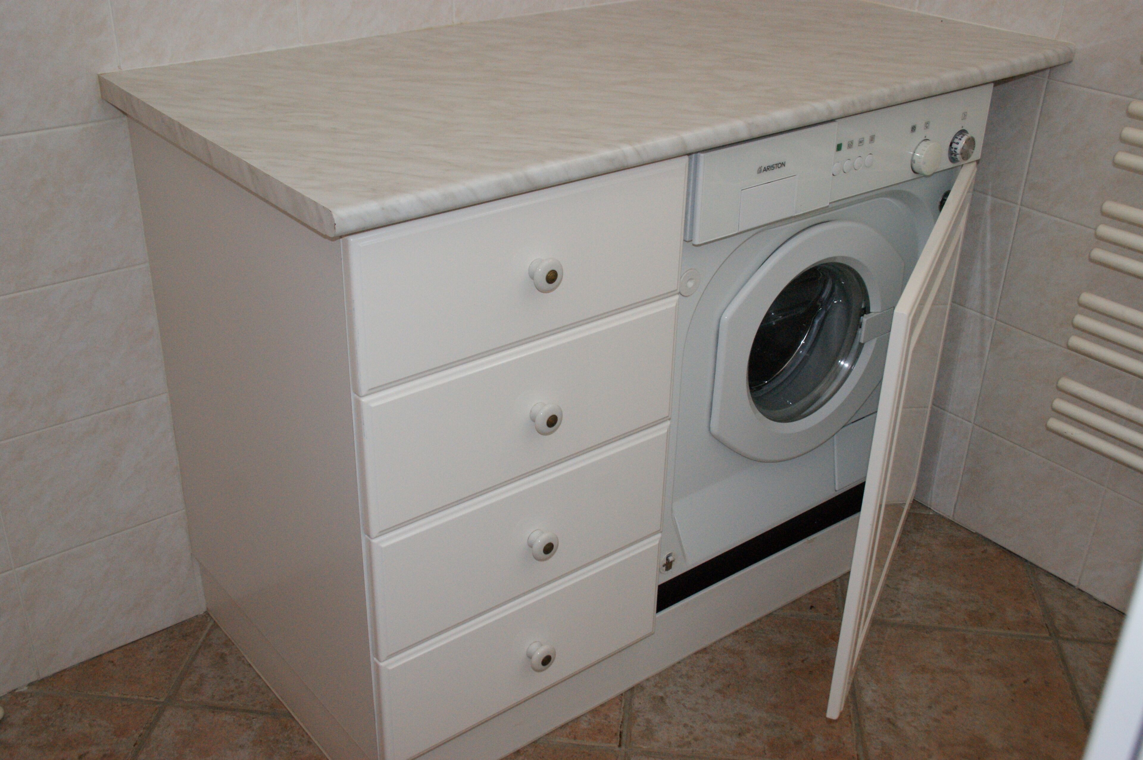 A compact, white laundry room with a built-in washing machine and a countertop.