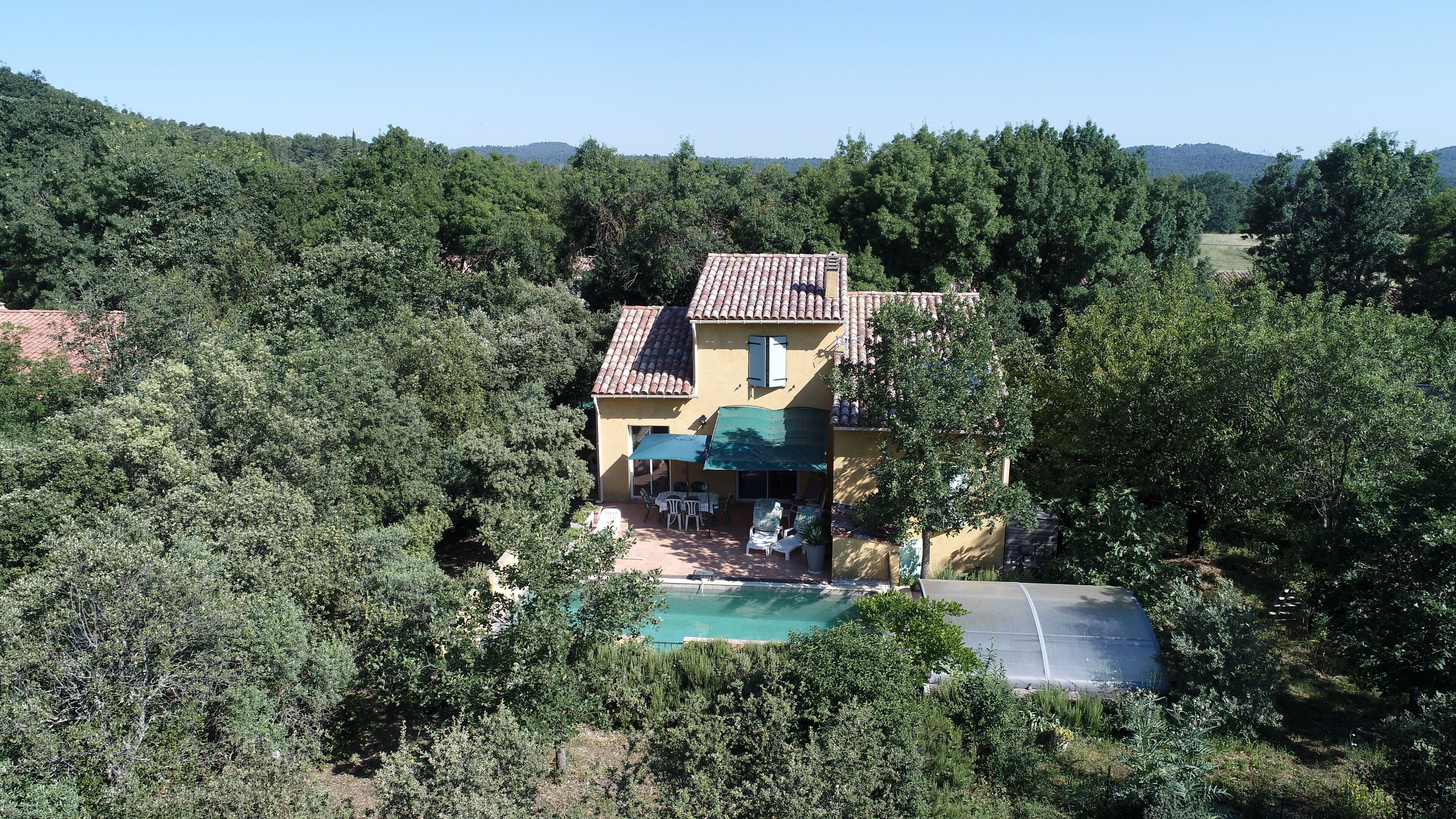 A house with a tiled roof, a swimming pool, and a patio area with outdoor furniture.