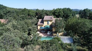 Uma casa com telhado em tijolos, piscina e área de varanda com móveis de exterior.
