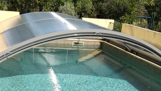 A clear indoor swimming pool with a curved edge, surrounded by trees.