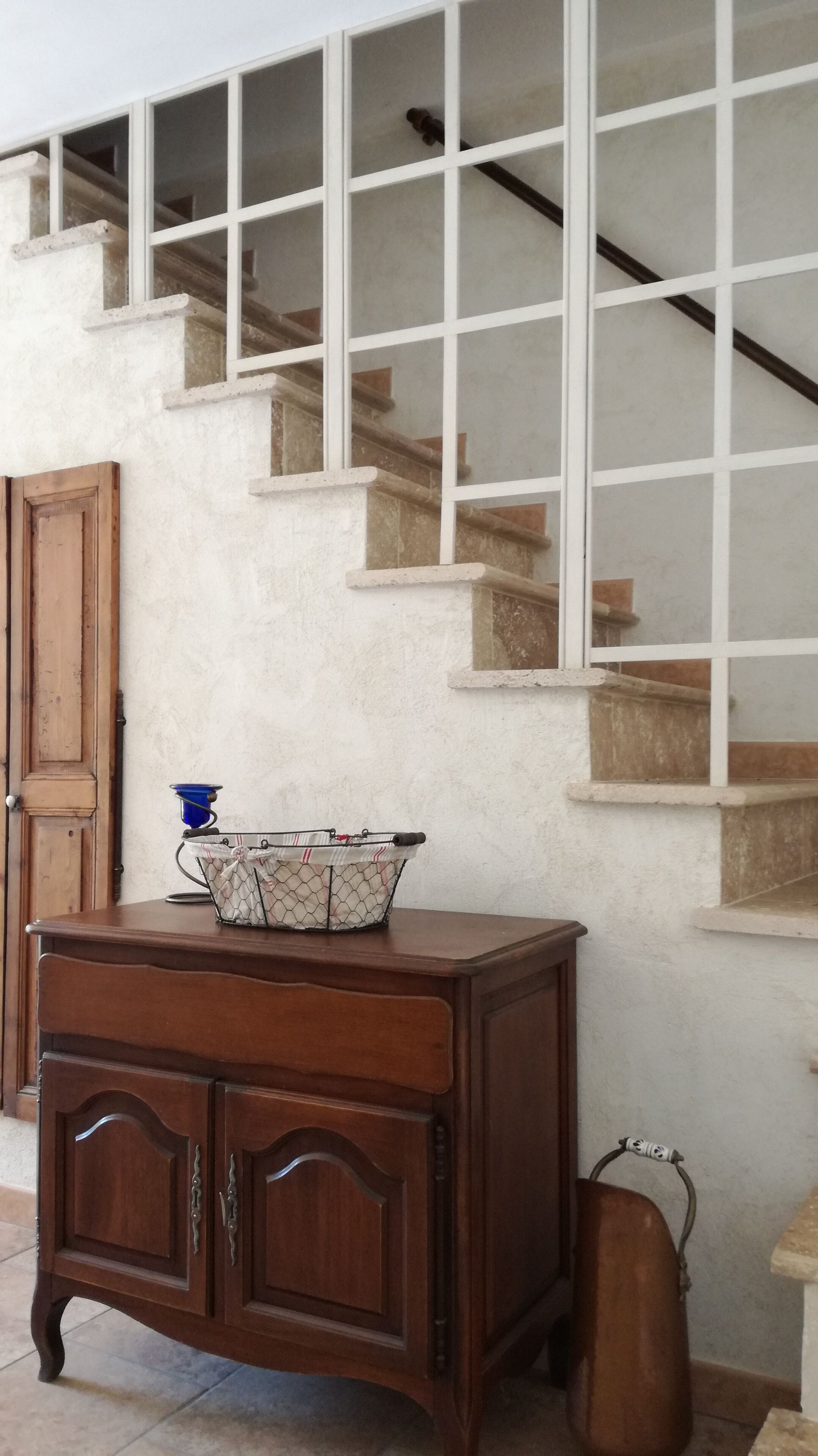 A wooden cabinet with drawers and a metal basket on top, positioned in front of a staircase with white railings and wooden steps.