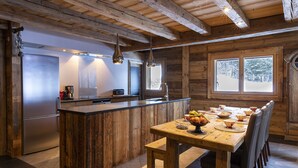 A rustic kitchen with a wooden island, stainless steel appliances, and a dining area with a wooden table and chairs.