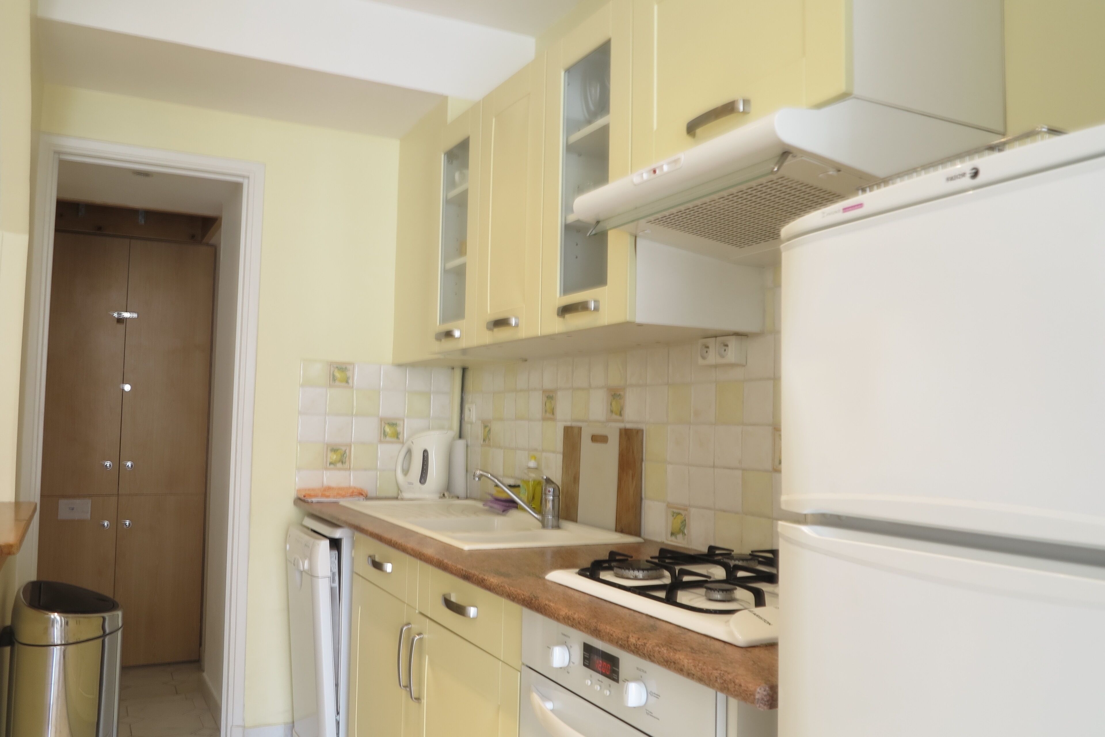 A kitchen with yellow cabinets, a stove, a sink, and a trash can.