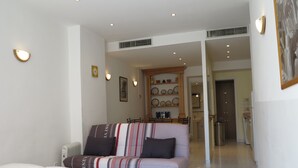 Un saló modern amb un sofà, un radiador i una zona de menjador amb una estant de plats.