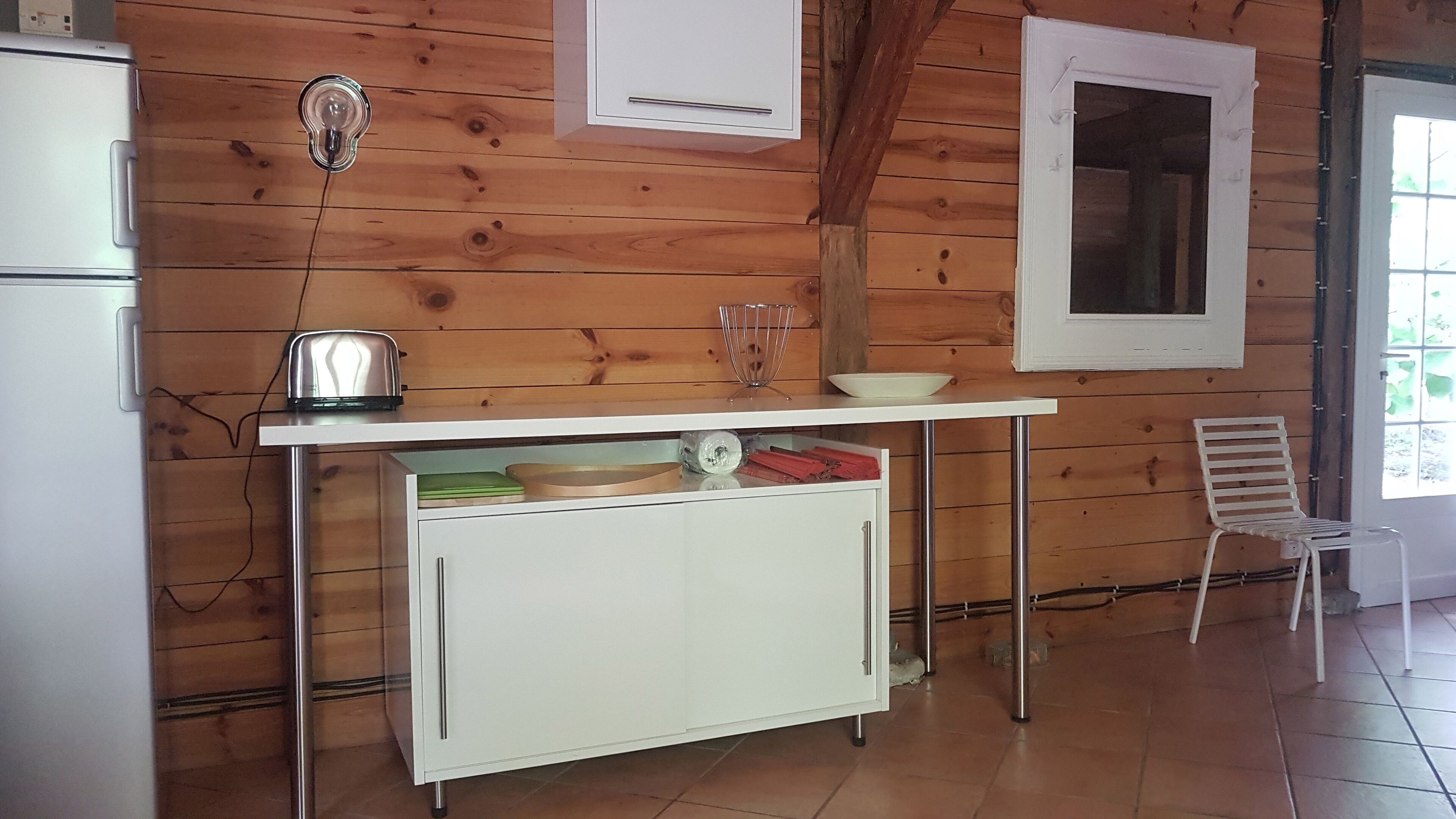 A compact kitchen with a white countertop, a small refrigerator, and a wooden wall.