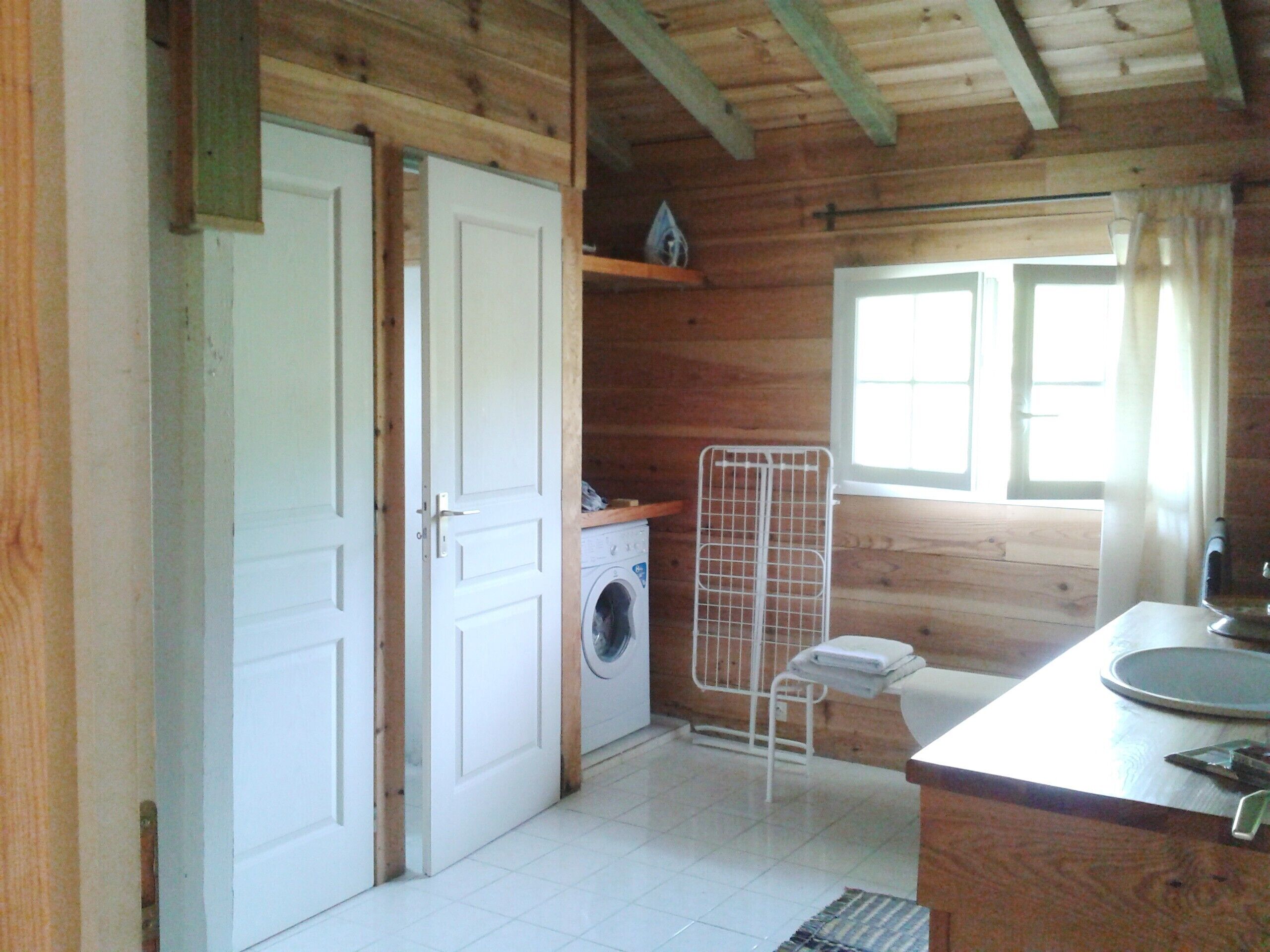 Une petite cabane en bois  équipée d’une machine à laver, d’un étendoir et d’un évier.