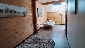 A bedroom with a sloped ceiling, wooden walls, a bed with a star-patterned bedspread, a chair, and a small table. - Cottages to Orient - Chalet Nature (Géraudot)