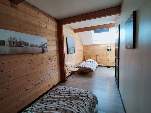 Une chambre avec un plafond en pente, des murs en bois, un lit recouvert d’une couvre-lit à motifs étoilés, une chaise et une petite table.