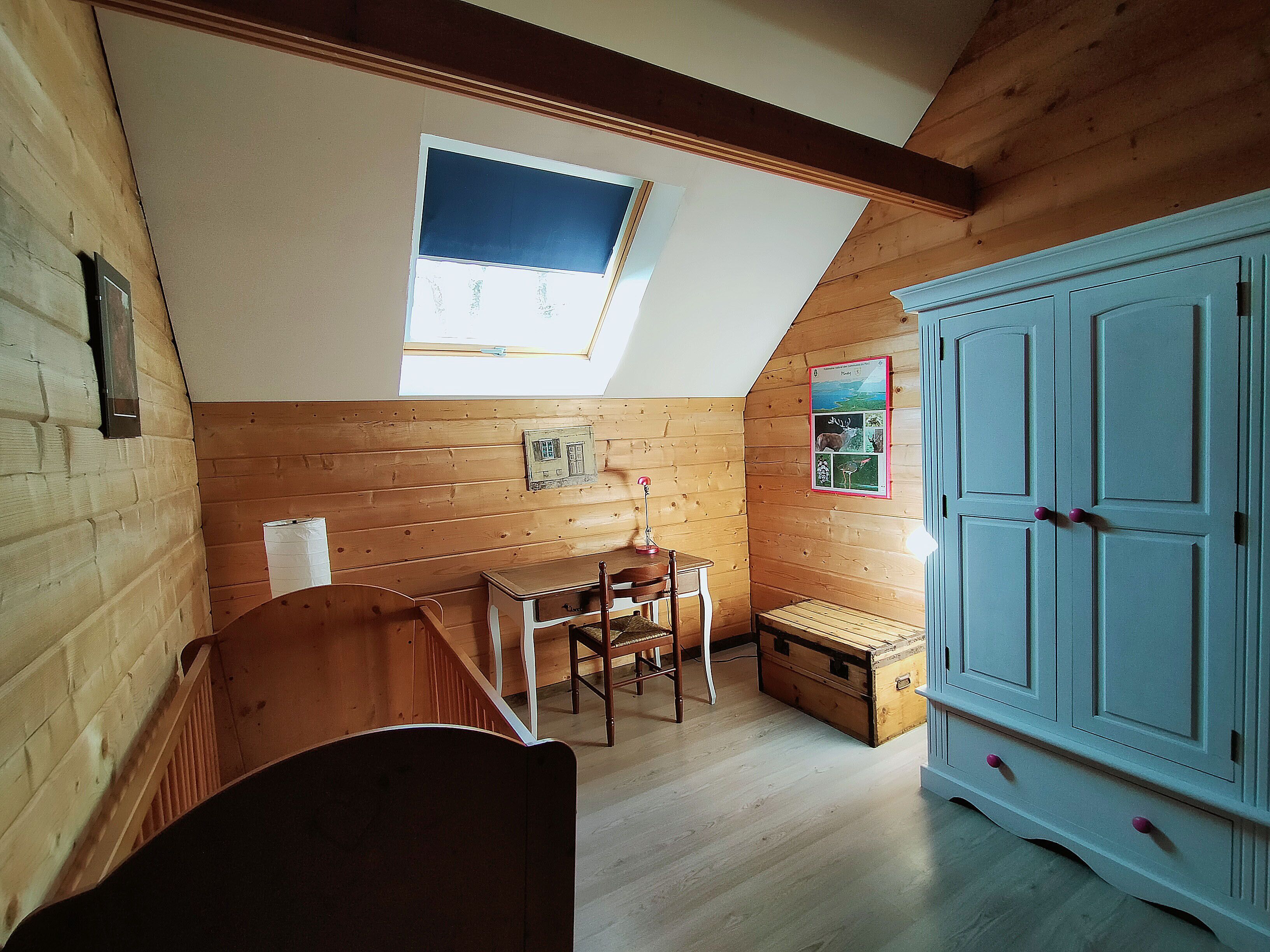 Een kamer met een schuine kap, houten wanden, een klein tafeltje met stoelen, een kast en een raam met uitzicht.